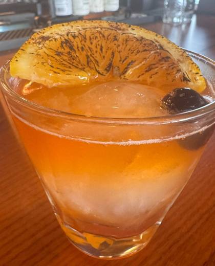 A cocktail over a large ice cube, garnished with a dehydrated orange wheel