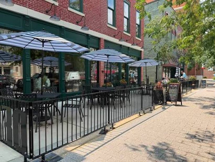 Sidewalk tables under striped umbrellas outside the brick storefront of 1830 Chophouse on Main Street