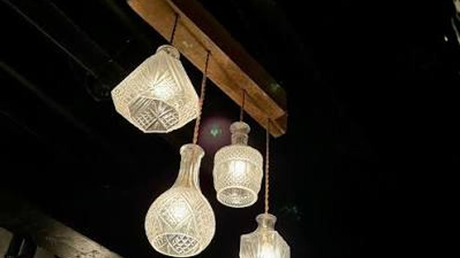 Cut-glass decanters hung from a timber beam as pendant lights, glowing against a dark ceiling