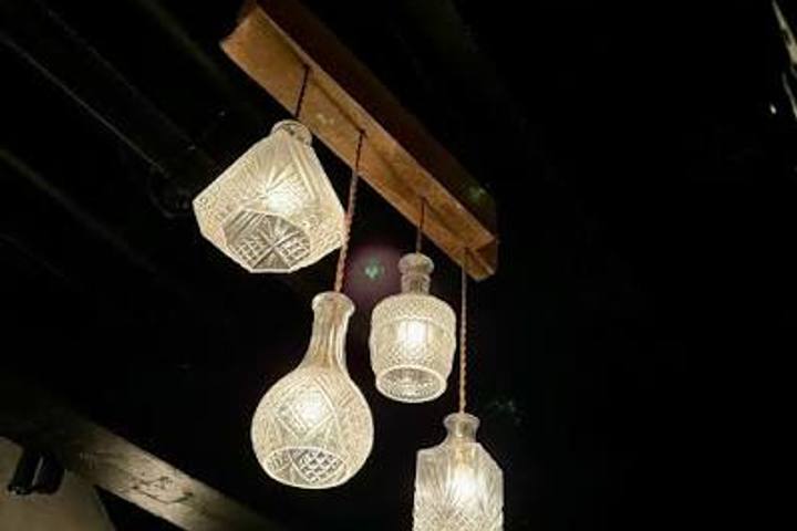 Cut-glass decanters hung from a timber beam as pendant lights, glowing against a dark ceiling
