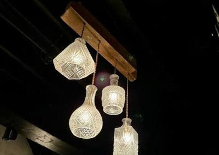 Cut-glass decanters hung from a timber beam as pendant lights, glowing against a dark ceiling