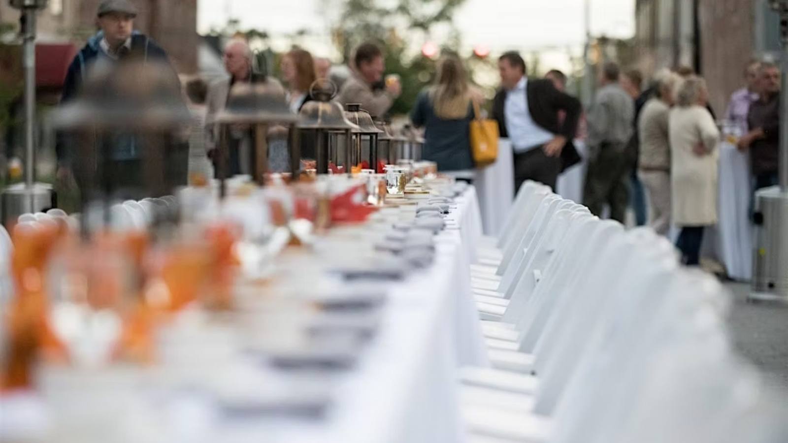 A long banquet table set down the middle of Main Street with neighbors gathering