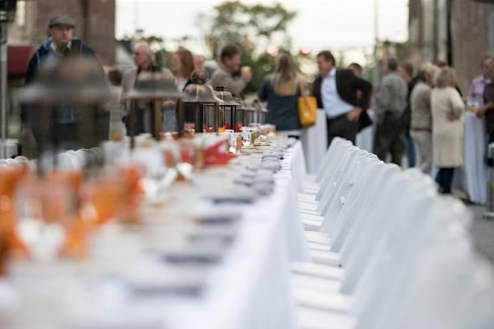 A long table set down the middle of the street at dusk, lanterns lit along it and guests gathered at either side