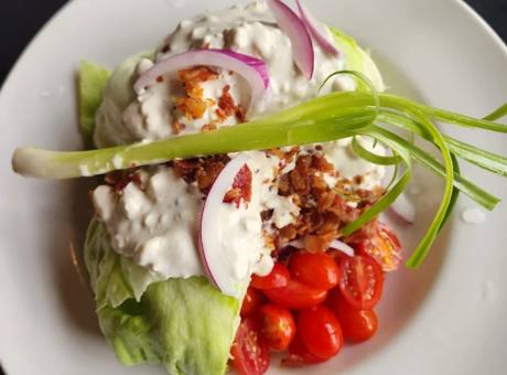 A wedge salad with blue cheese dressing, red onion and bacon